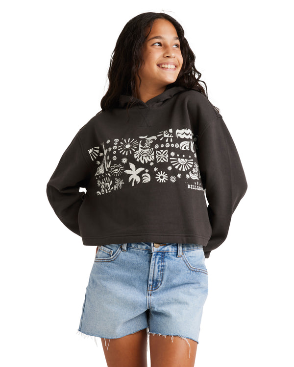 Smiling young woman wearing a black Billabong hoodie with white tropical graphics, paired with distressed denim shorts.