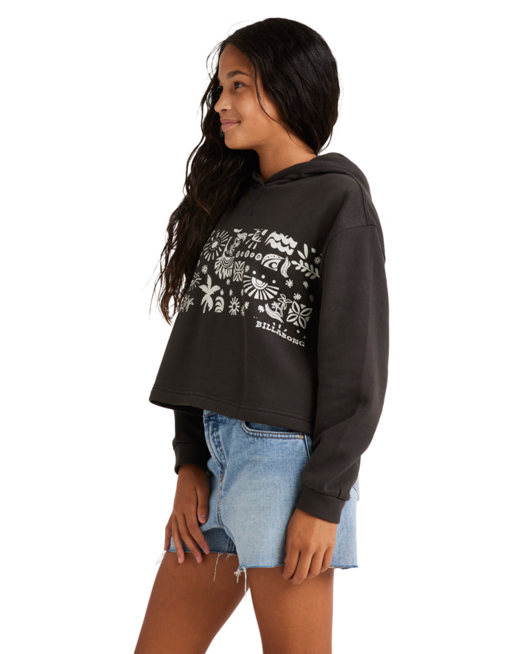 Side view of a woman wearing a black Billabong hoodie with white graphic prints, paired with light-wash denim shorts