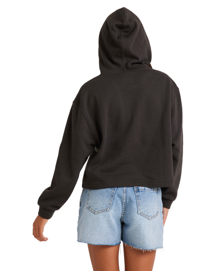 Back view of a woman wearing a black Billabong hoodie with the hood up, paired with light-wash distressed denim shorts.