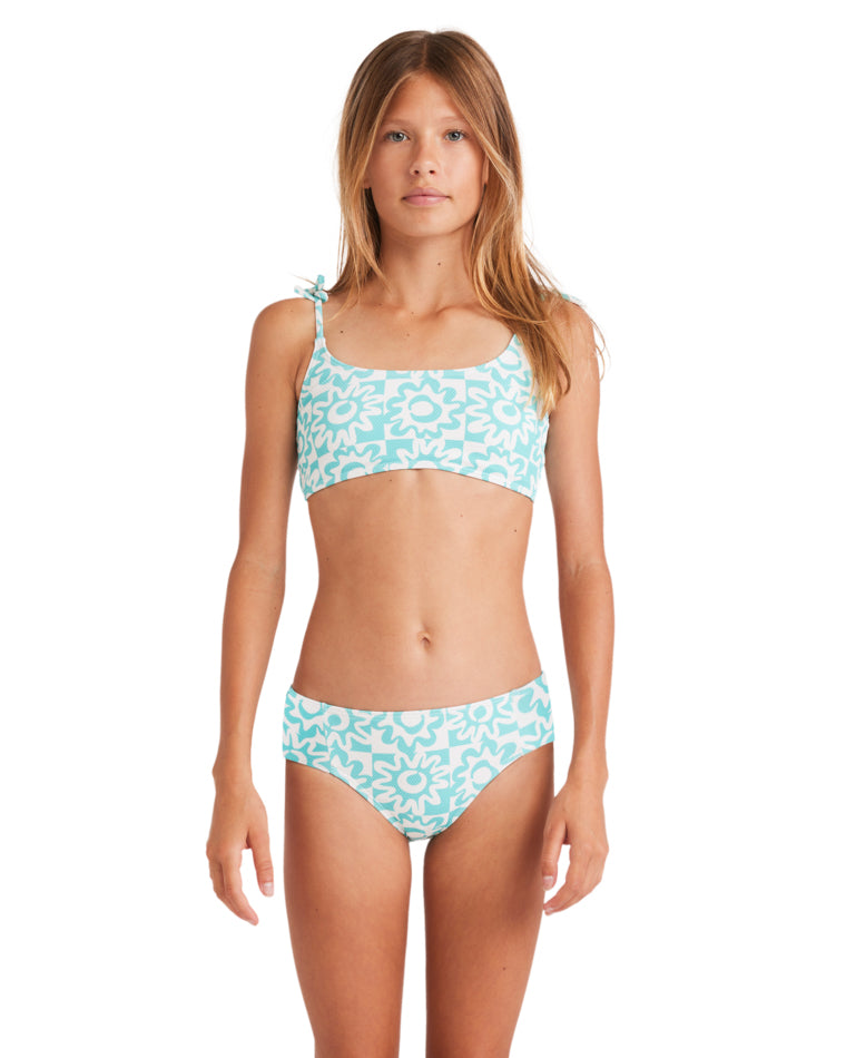 Girl wearing a turquoise and white floral print bikini with tie-shoulder straps, standing front-facing.