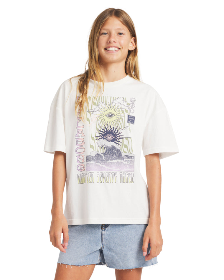 Girl wearing a white oversized t-shirt with a psychedelic Billabong graphic on the front, paired with light-wash denim shorts.