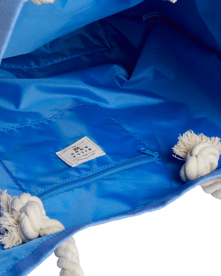 Interior view of a light blue Billabong tote bag showing a zippered pocket, white rope handles, and blue lining with a fabric brand label.
