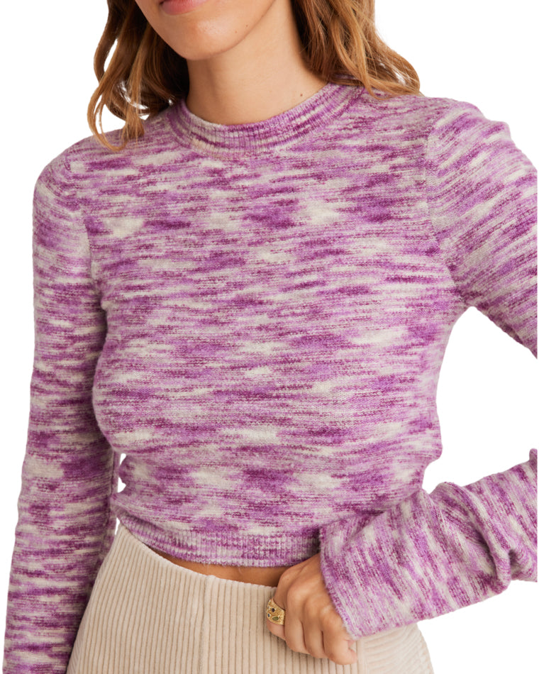 Close-up of a marled pink and white cropped sweater with long sleeves, paired with high-waisted ribbed beige pants.
