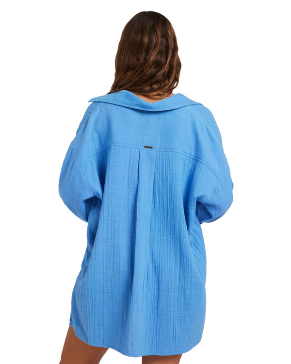 Back view of model wearing a blue oversized button-up shirt with a relaxed fit and textured fabric, draping loosely.