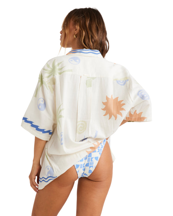 Back view of an oversized white button-up shirt featuring colorful tropical prints, worn over a blue and white bikini.