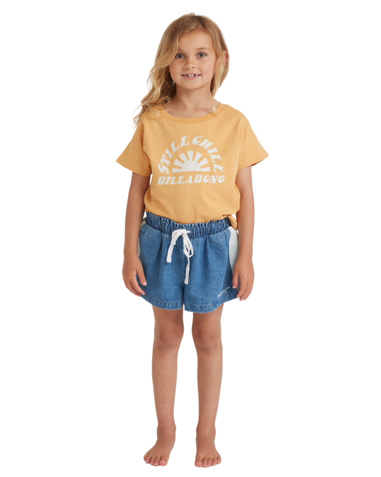 Front view of a girl wearing a yellow "Still Chill Billabong" t-shirt with blue elastic waist denim shorts and a white drawstring.