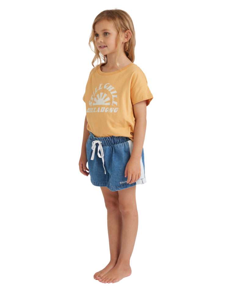 Side view of a girl in a yellow Billabong t-shirt and light-wash denim shorts featuring contrast white side panels and drawstring waist.