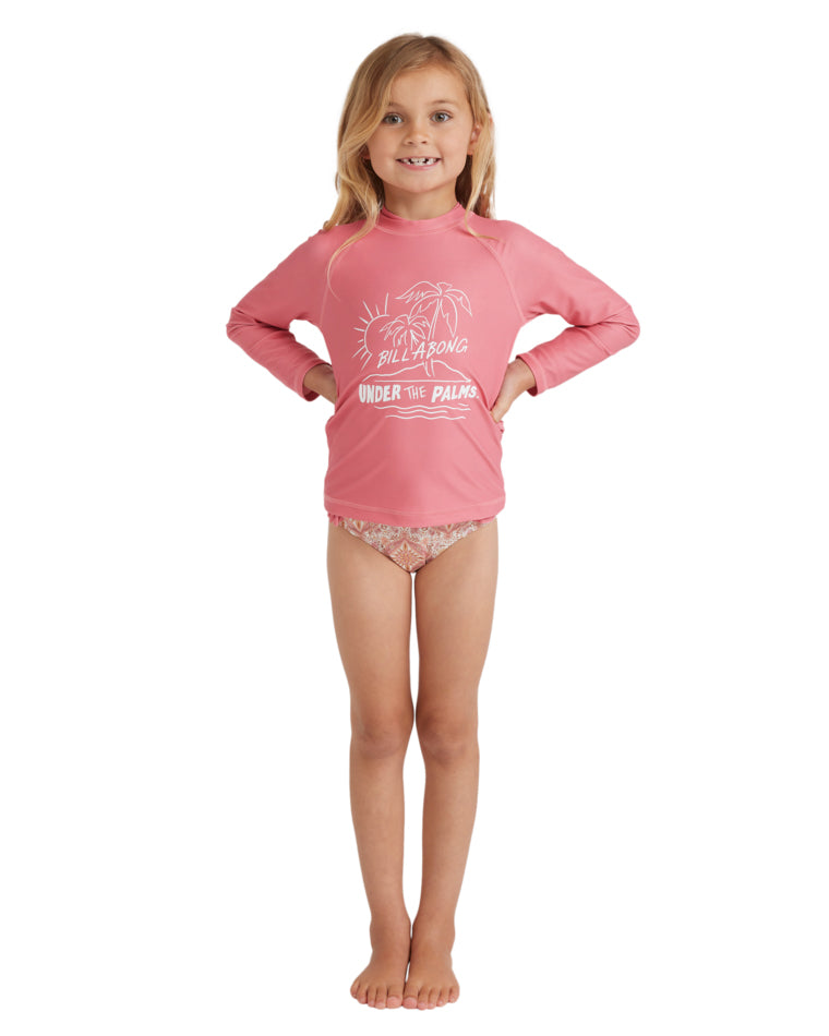 Young girl front view wearing a pink long sleeve Billabong rash vest with “Under the Palms” print and floral bikini bottoms.
