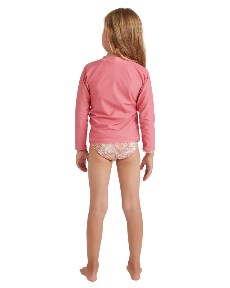 Young girl back view wearing a pink long sleeve rash vest and floral bikini bottoms.