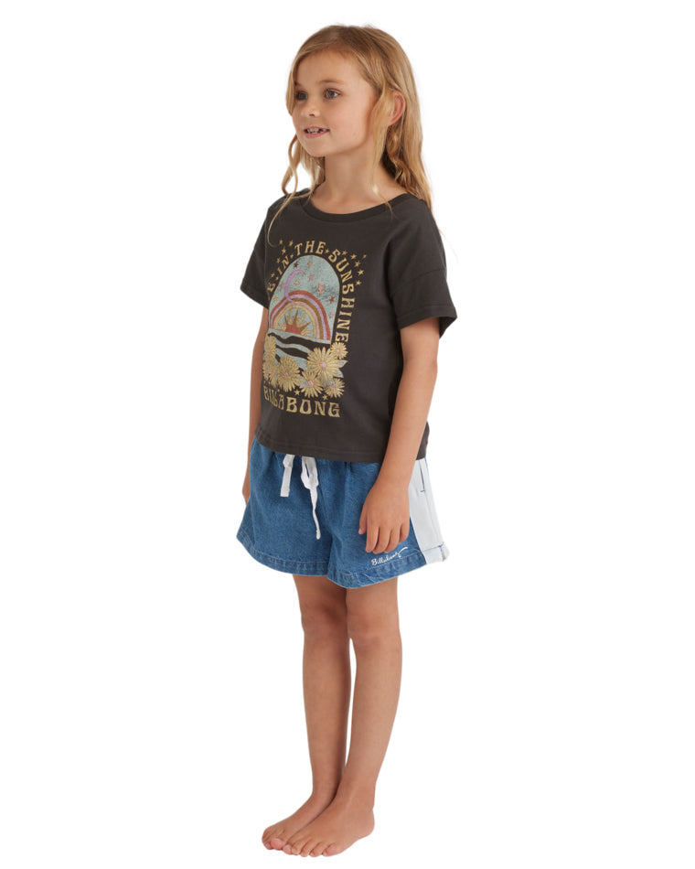 Side profile of a girl wearing a black “Live in the Sunshine” Billabong t-shirt and drawstring denim shorts