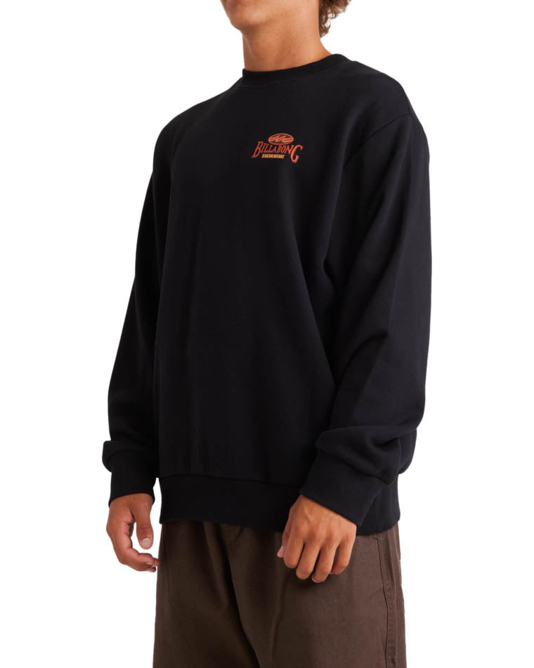 Side view of a model wearing a black Billabong crewneck sweatshirt with a small red and yellow logo on the chest.