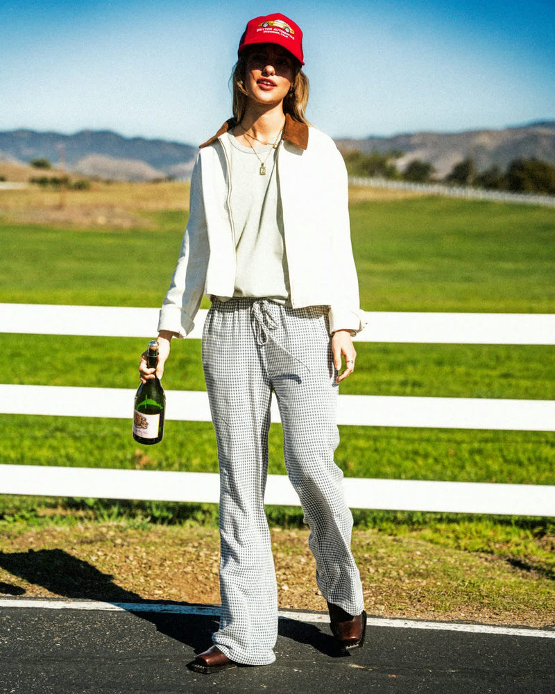 Woman wearing relaxed-fit gingham pants with a drawstring waist, styled with boots and a cropped jacket in a countryside setting.