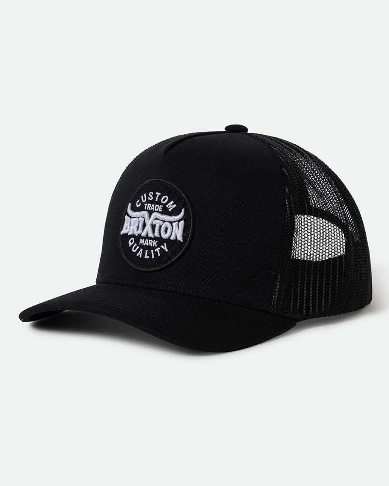 A black trucker cap featuring a mesh back and a front patch with "Custom Brixton Trade Mark Quality" text in white embroidery.