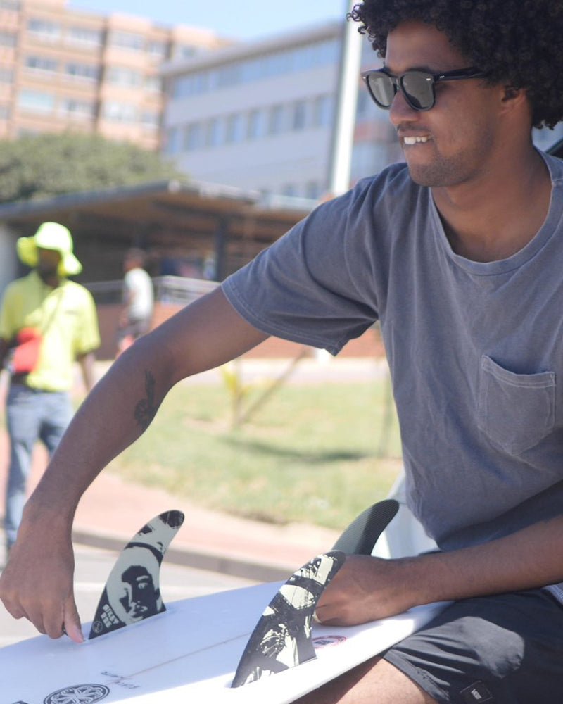 Surfer installing black and cream graphic fins with portrait design onto a white surfboard