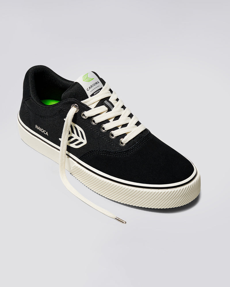 Black Cariuma Naioca sneaker with white laces, a green insole, and a textured off-white rubber sole, one lace undone.