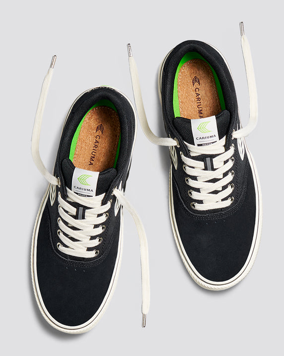 Top-down view of black Cariuma Naioca sneakers with white laces, cork insoles, and green lining accents.