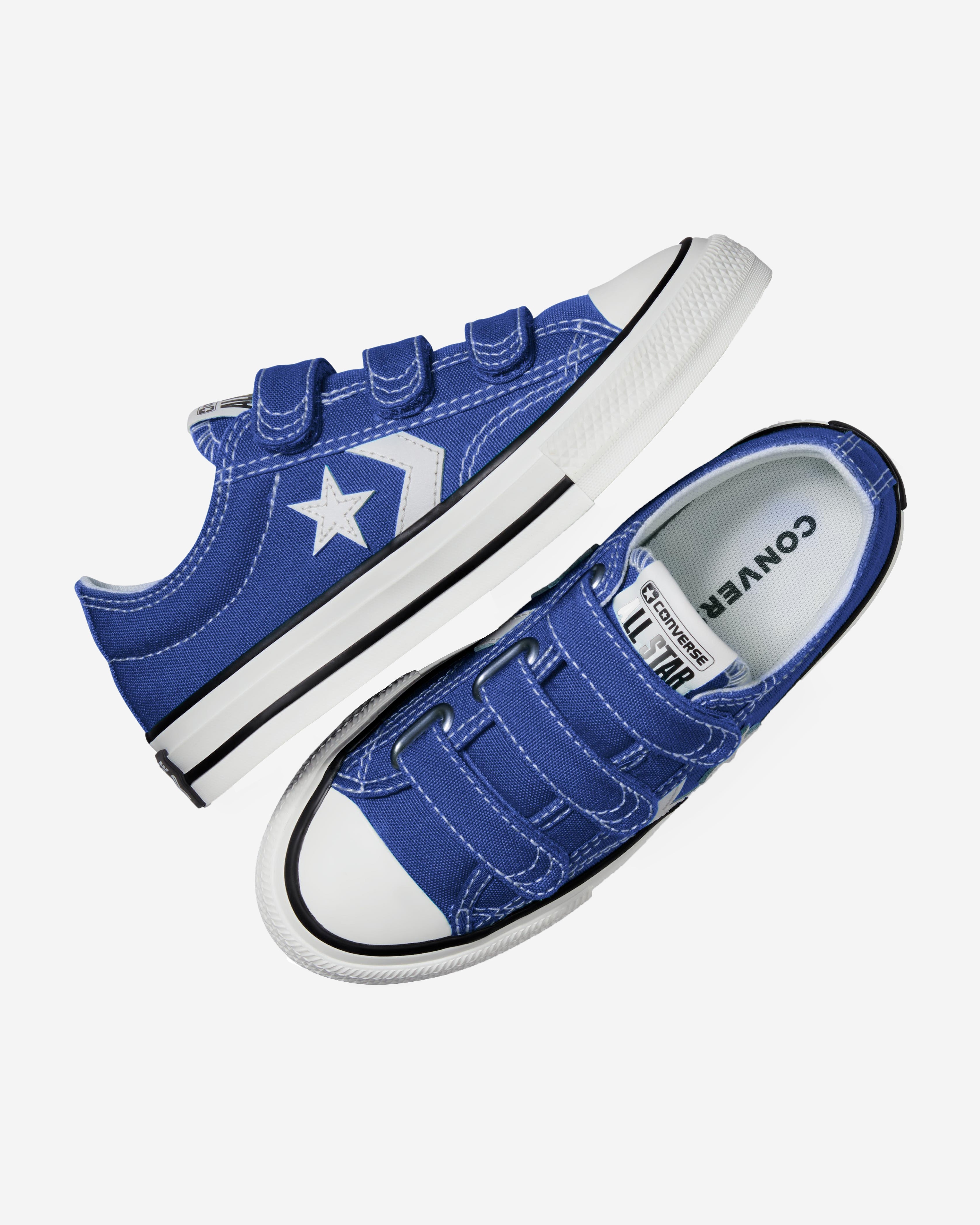 A pair of blue Converse Star Player sneakers with white accents and Velcro straps, displayed in a dynamic angled view.
