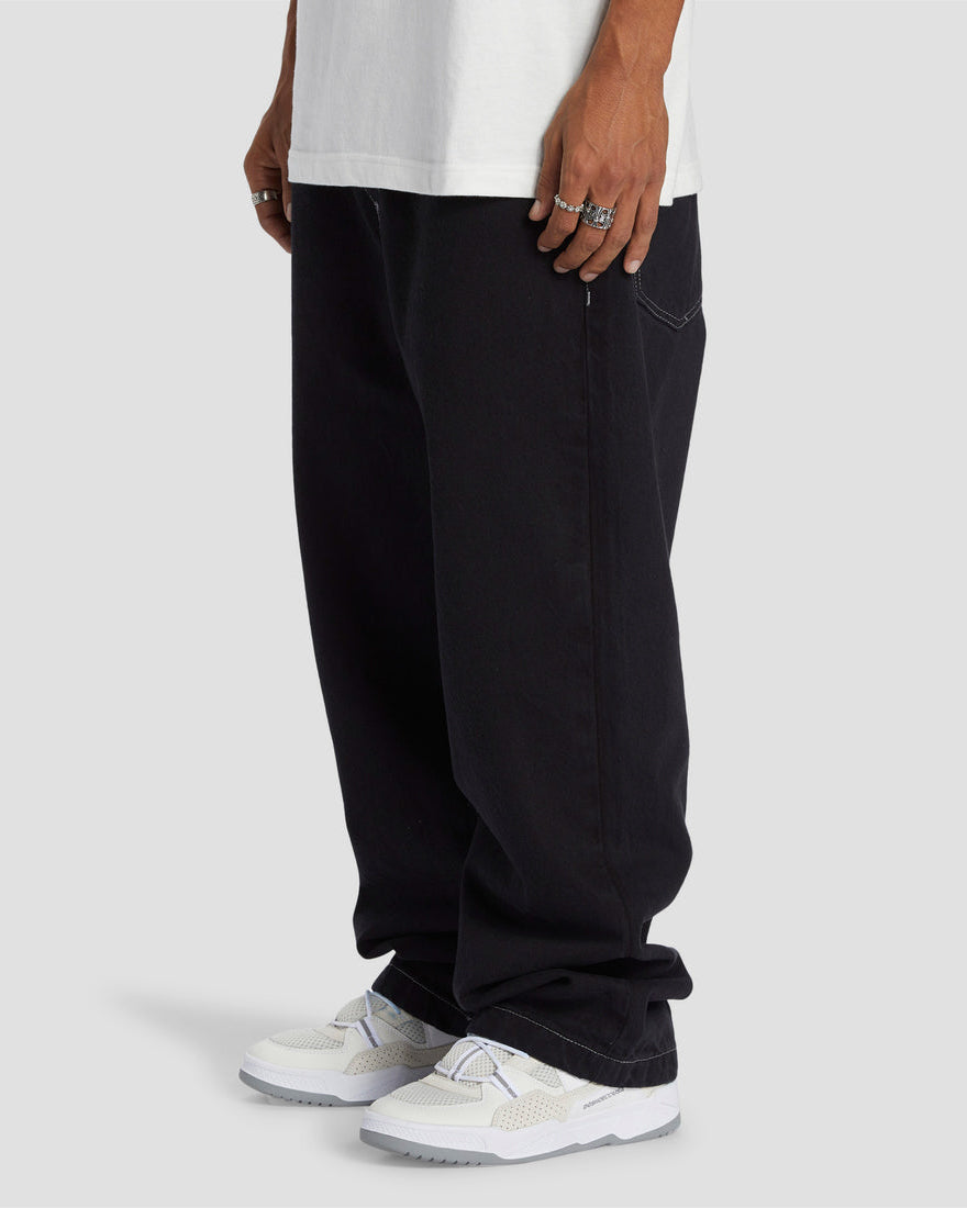 Man wearing baggy black jeans with white sneakers and silver rings