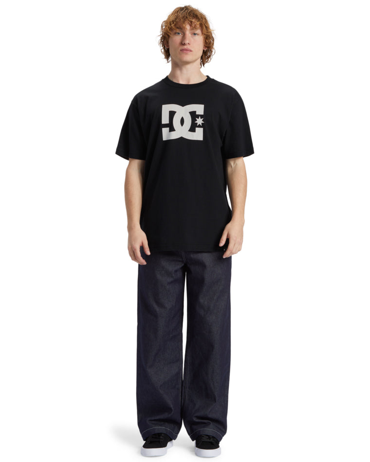 Model wearing black DC t-shirt with white logo and wide-leg dark denim jeans, front-facing full-body view.