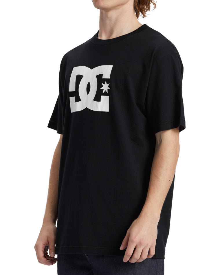 Side view of black DC t-shirt with oversized white logo on chest, worn with relaxed jeans.