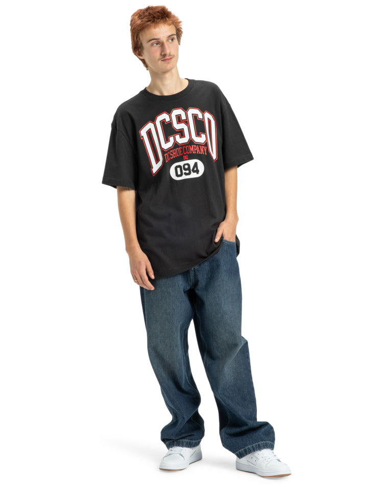 Model wearing black DC Shoes graphic tee with relaxed jeans and white sneakers.