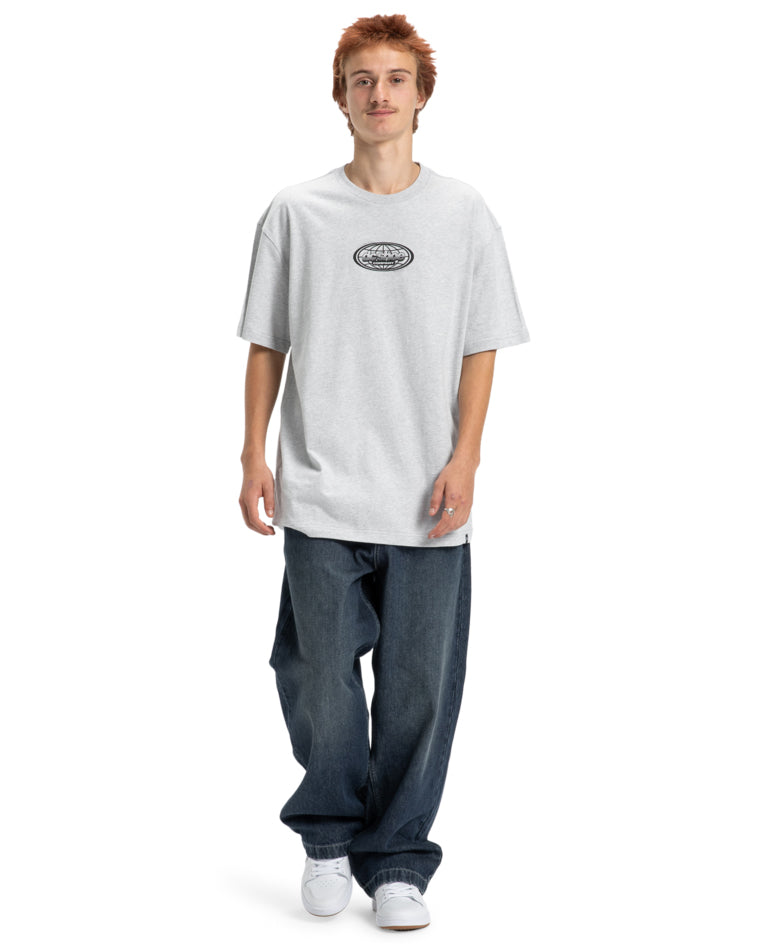 Model wearing grey DC Shoes tee with relaxed jeans and white sneakers.