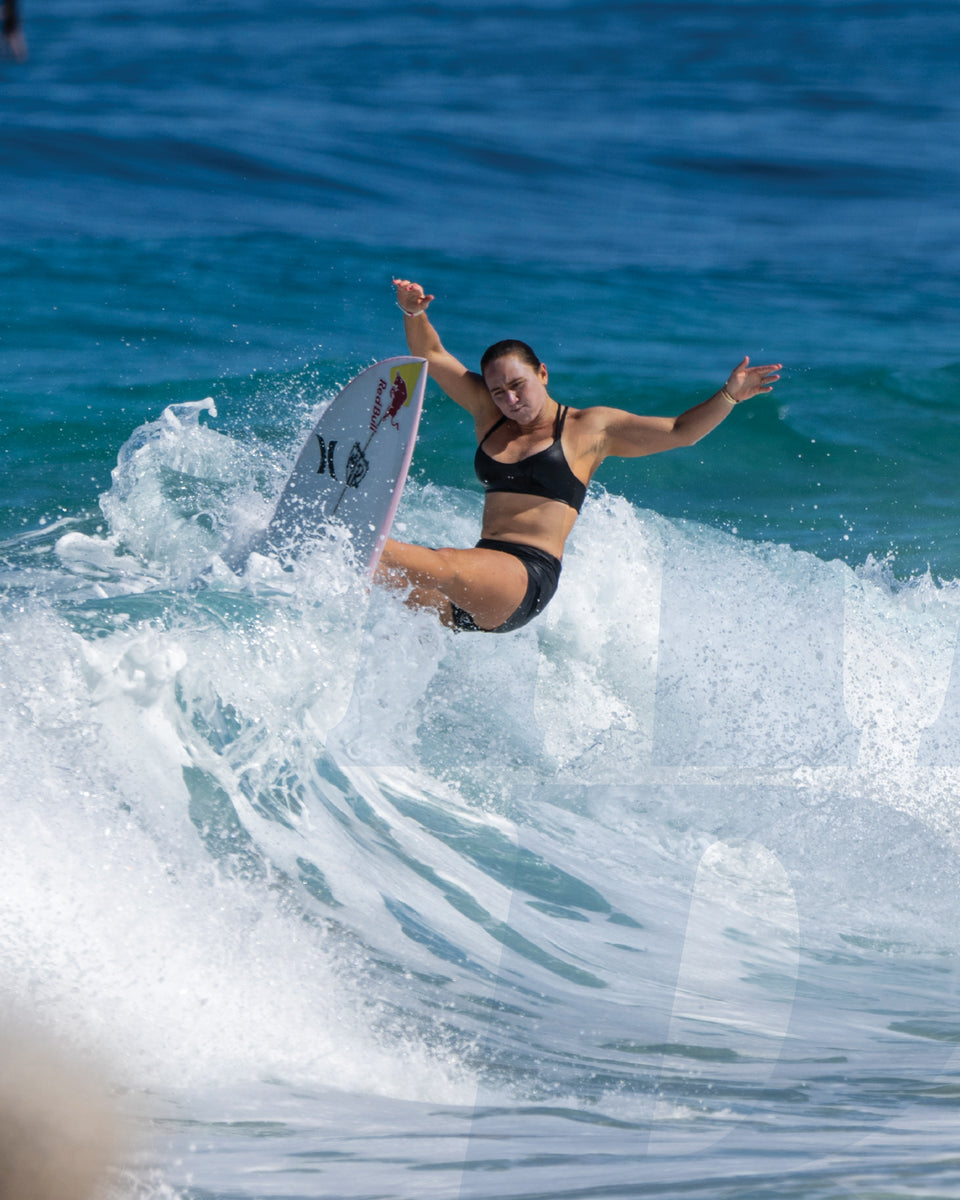 Female surfer performing a top turn on a wave wearing black swimwear with ocean spray around her board