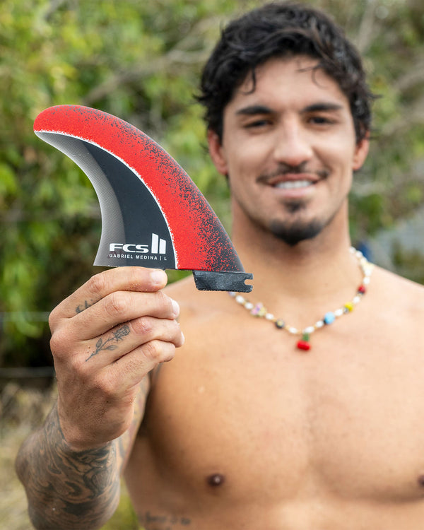 Surfer holding FCS II Gabriel Medina fin, smiling and showcasing its unique red and black pattern.