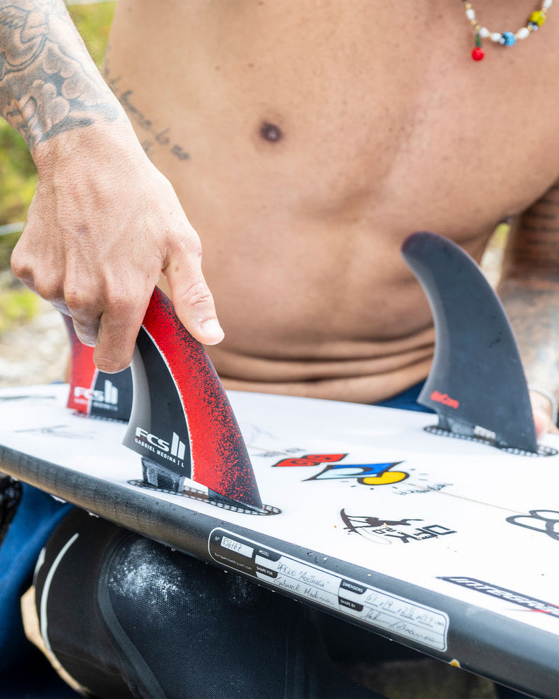 Installing FCS II Gabriel Medina fins onto a white surfboard with signature artwork and grip pad.