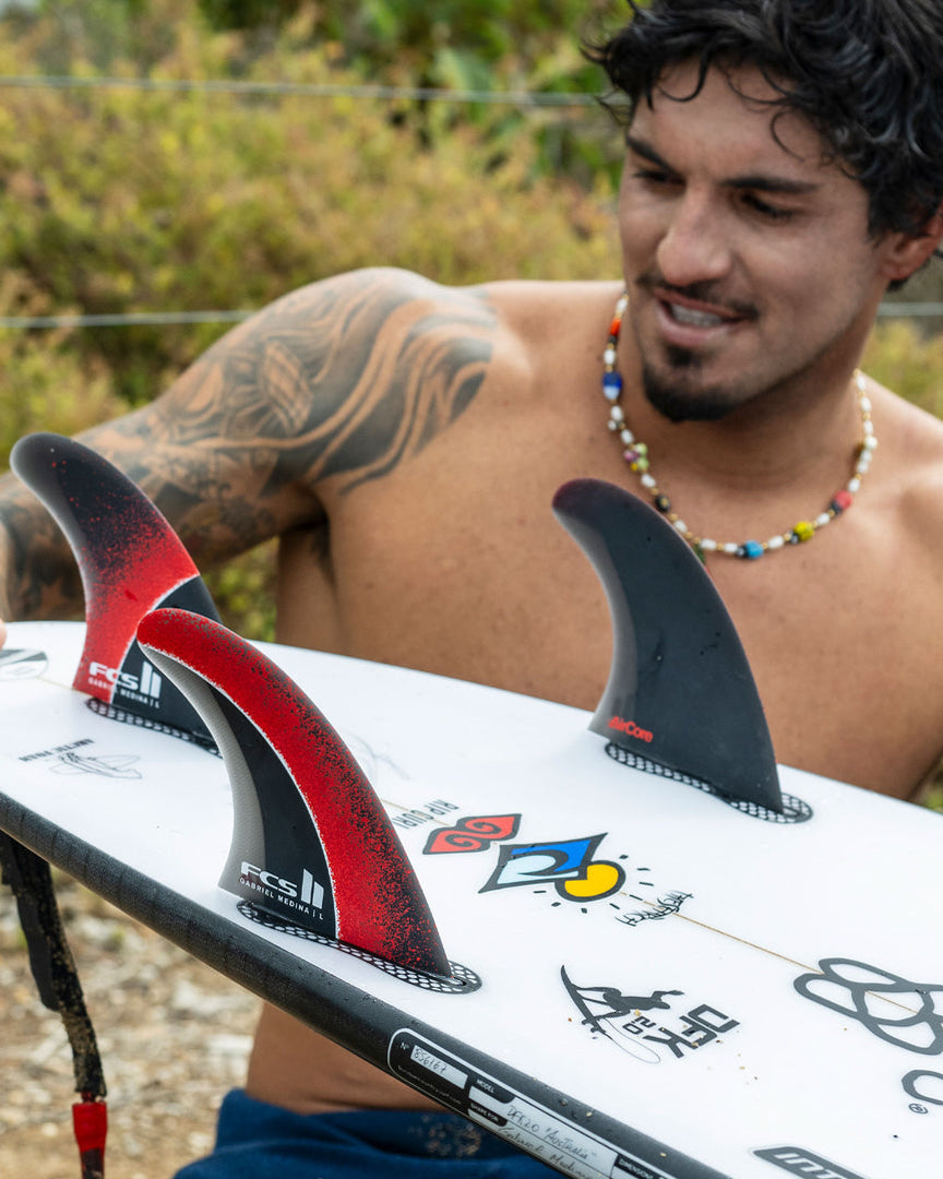 Surfer checking FCS II Gabriel Medina fins installed on a white shortboard with logos and artwork