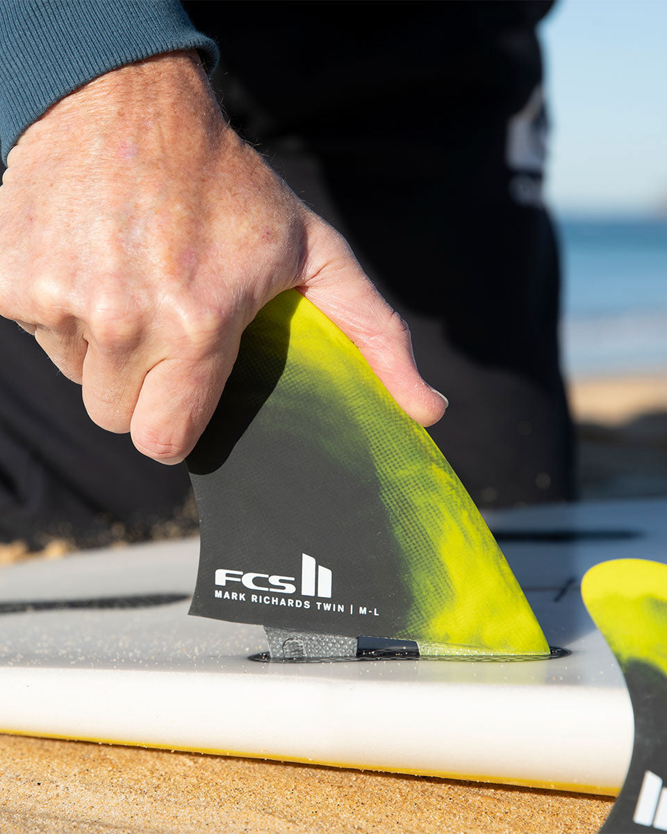 Hand installing FCS II Mark Richards Twin fin into surfboard, showing clear fit and tool-less design system.