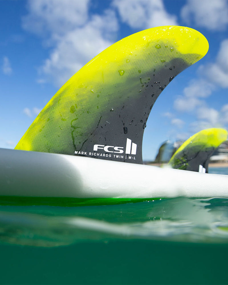 FCS II Mark Richards Twin fins in action on a board in the ocean, with water droplets and vibrant yellow colour visible.
