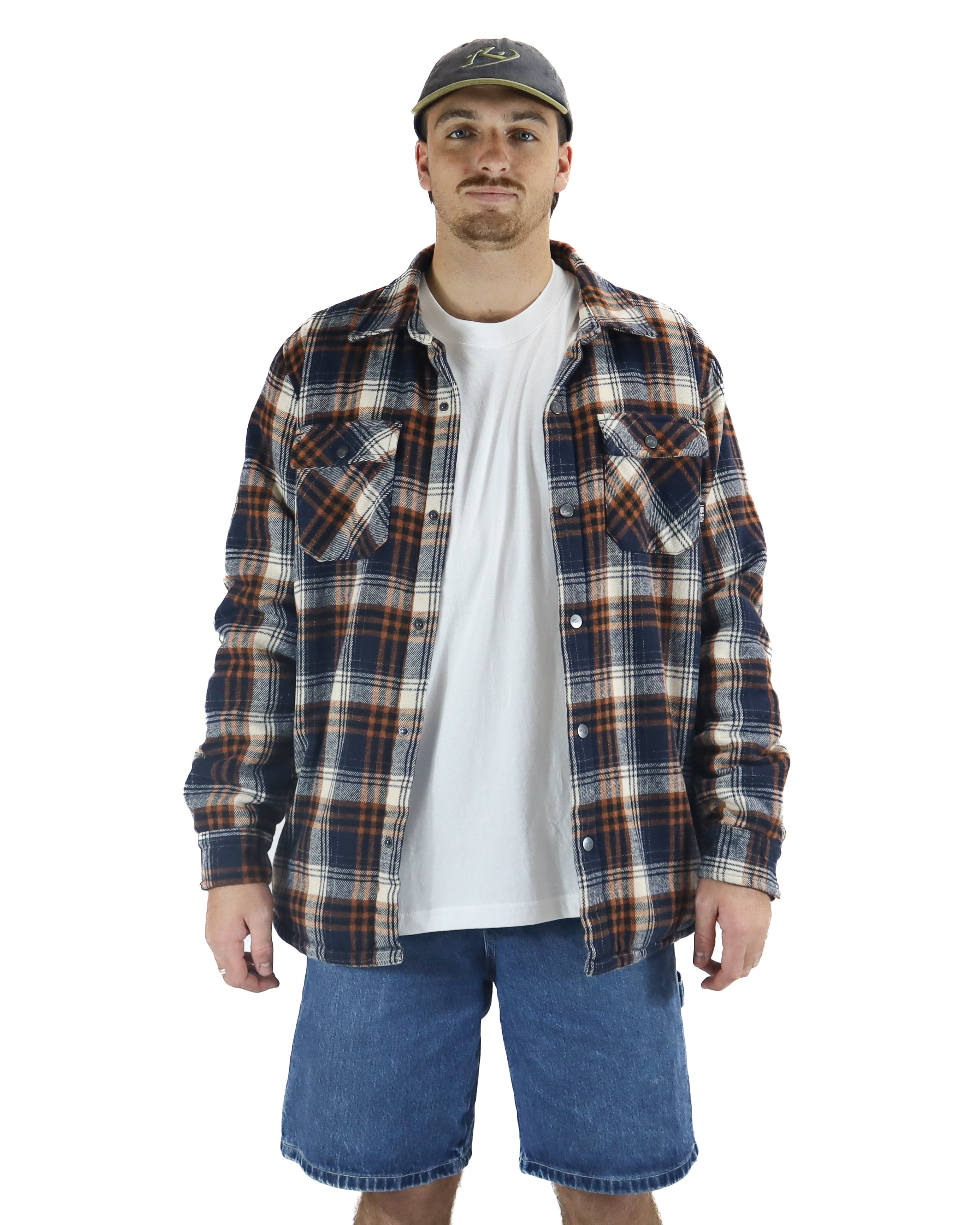 Man wearing navy, brown and white plaid flannel shirt over a white tee with denim shorts and a cap