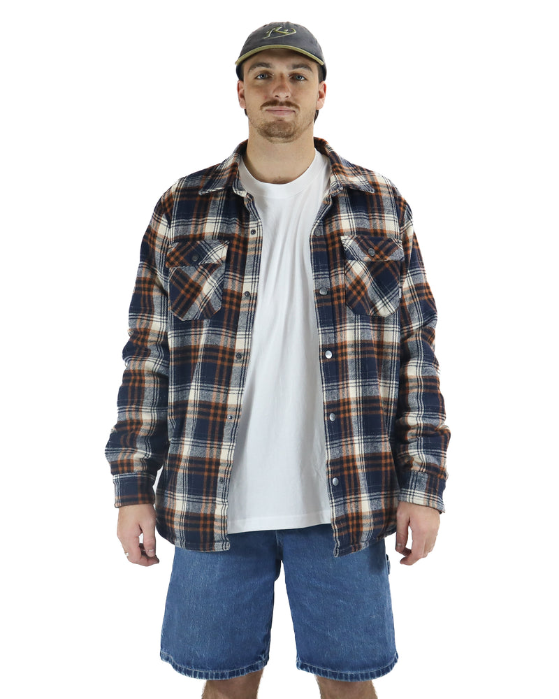 Man wearing navy, brown and white plaid flannel shirt over a white tee with denim shorts and a cap