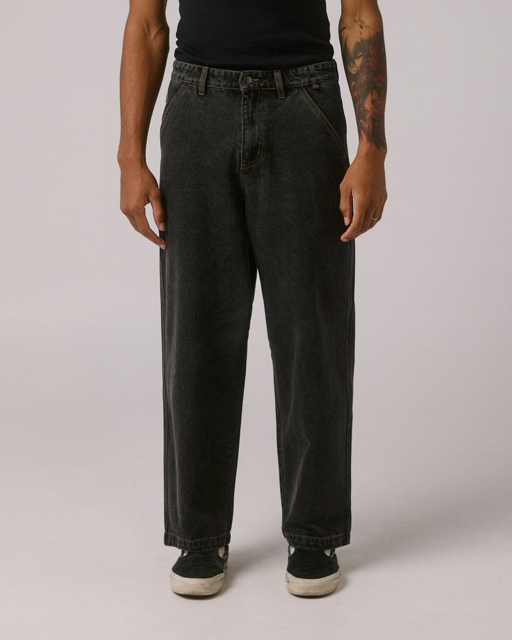 Front view of loose fit black jeans with angled pockets, worn with black top and slip-on sneakers.