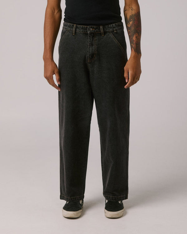 Front view of loose fit black jeans with angled pockets, worn with black top and slip-on sneakers.