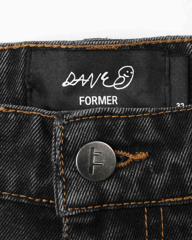 Close-up of Former jeans waistband with custom button and stitched brand label inside.