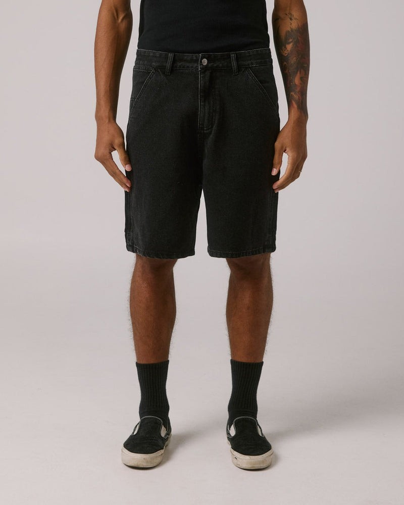 Front view of black denim shorts styled with a black tee and slip-on shoes
