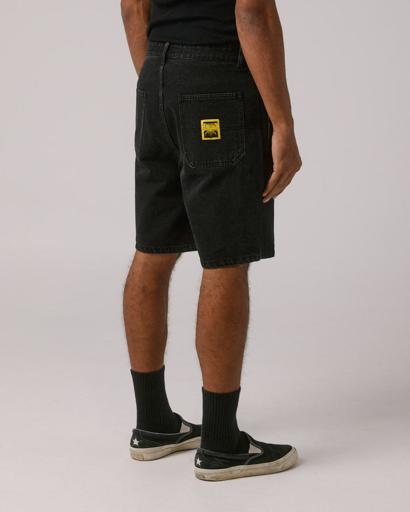 Back view of black denim shorts featuring a yellow patch on the pocket