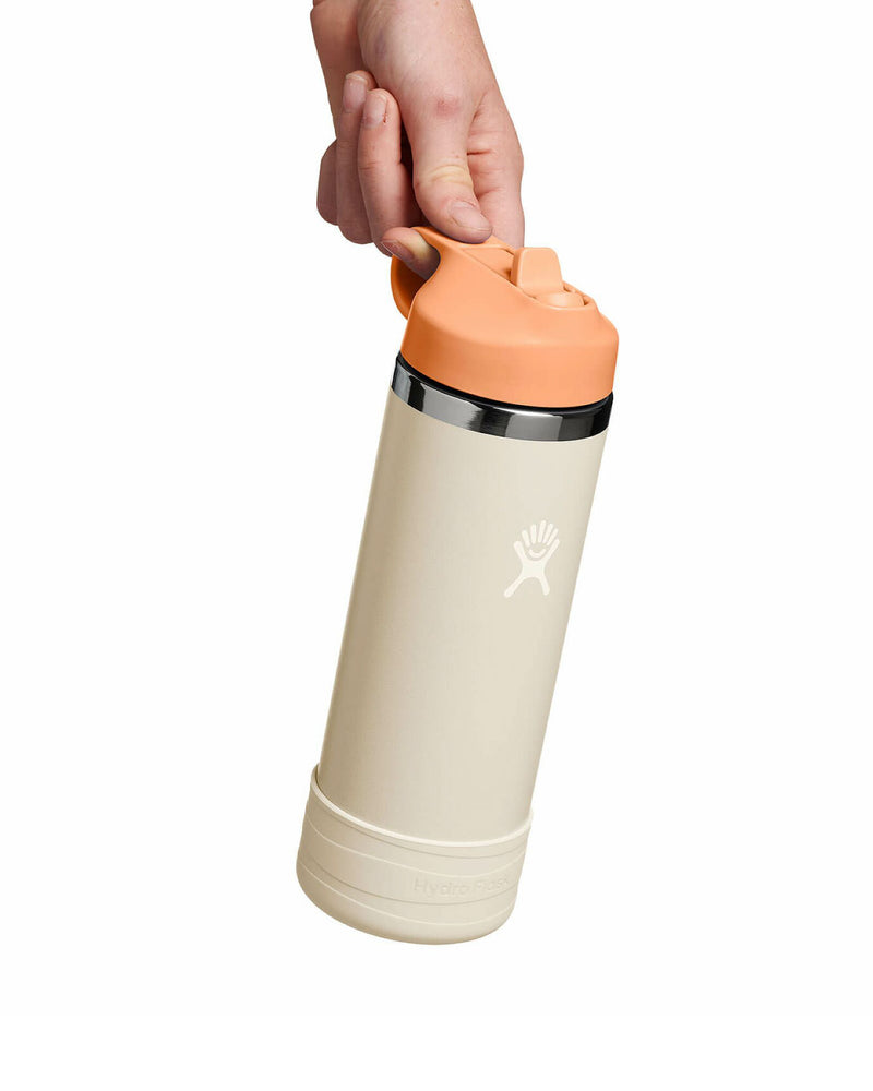 Hand holding beige and peach Hydro Flask bottle by carry loop on the lid.