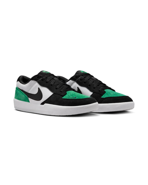 A pair of low-top sneakers with black, white, and green suede panels, featuring a black Nike swoosh and white rubber soles.