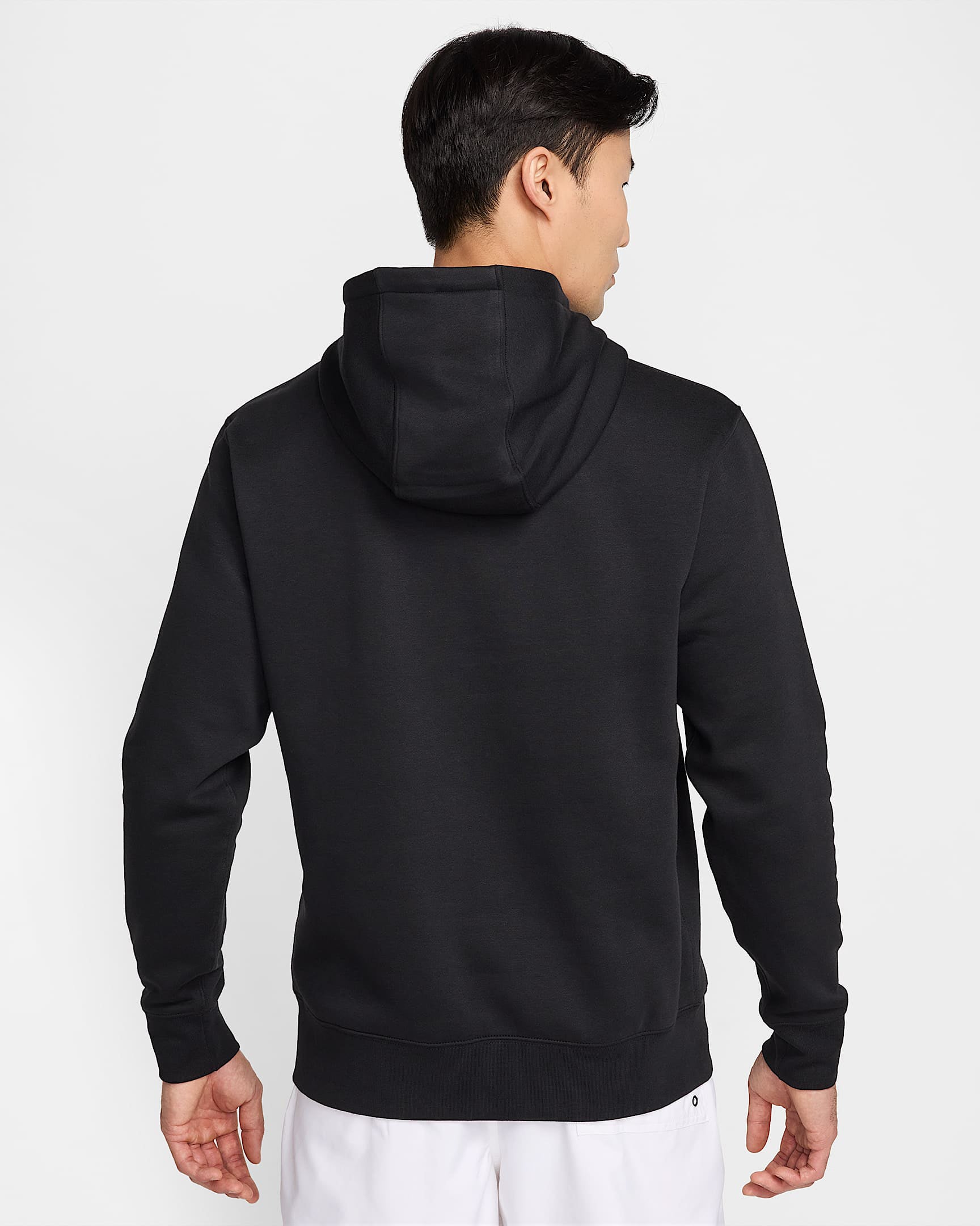 Back view of a black Nike hoodie with hood up, worn by a man in white shorts.