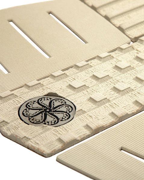 Close-up of textured centre arch with black circular traction logo on beige surfboard grip