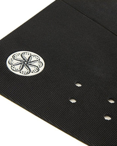 Close-up of black surfboard pad showing ribbed texture, grip holes, and embossed circular logo.
