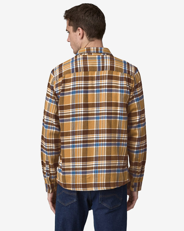 Back view of a man wearing a mustard, brown, and blue plaid flannel shirt with long sleeves, paired with dark blue jeans.