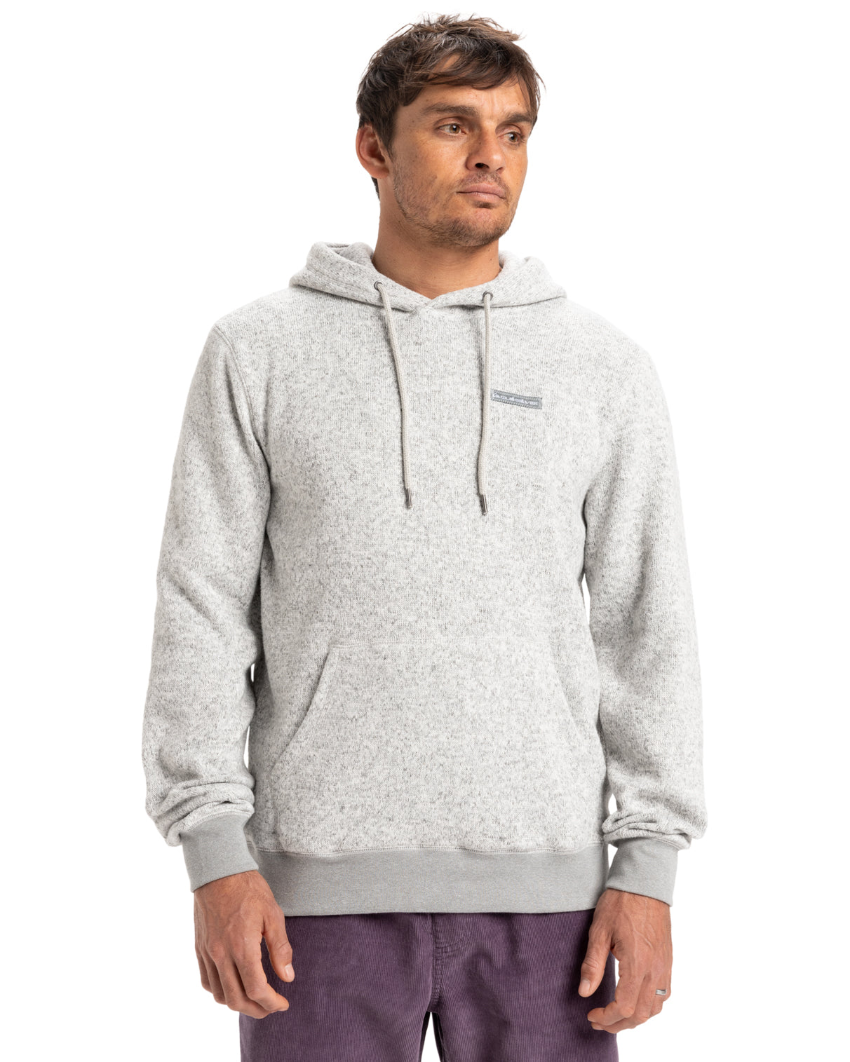 Man wearing a light gray hoodie with drawstrings and a small chest logo, paired with purple pants, looking to the side.