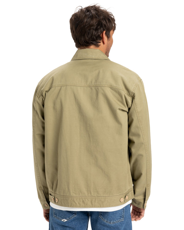 Back view of a man wearing a khaki Quiksilver jacket with adjustable buttoned hem, paired with a white t-shirt and jeans.