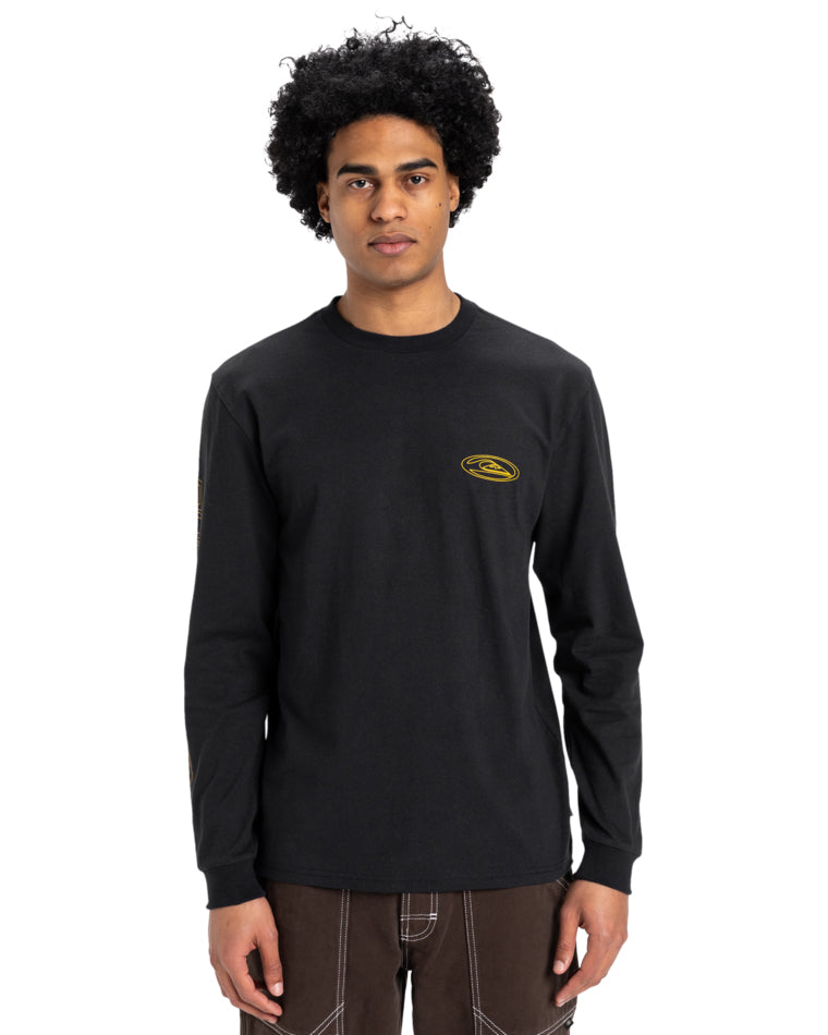 Model wearing a black long-sleeve T-shirt with a small yellow Quiksilver logo on the chest and subtle design details on sleeves.