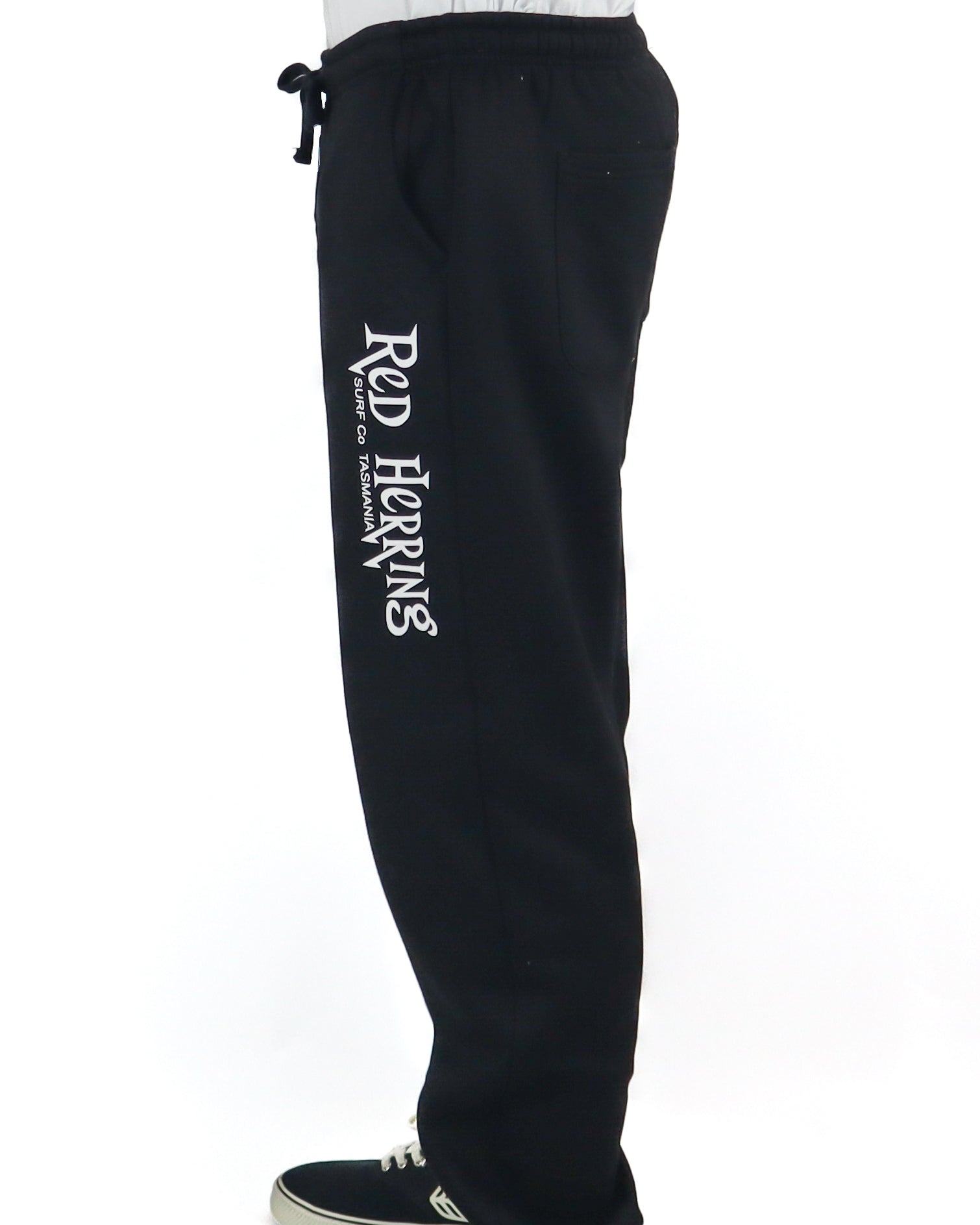 Side view of black track pants with bold Red Herring Surf Co. print down the leg