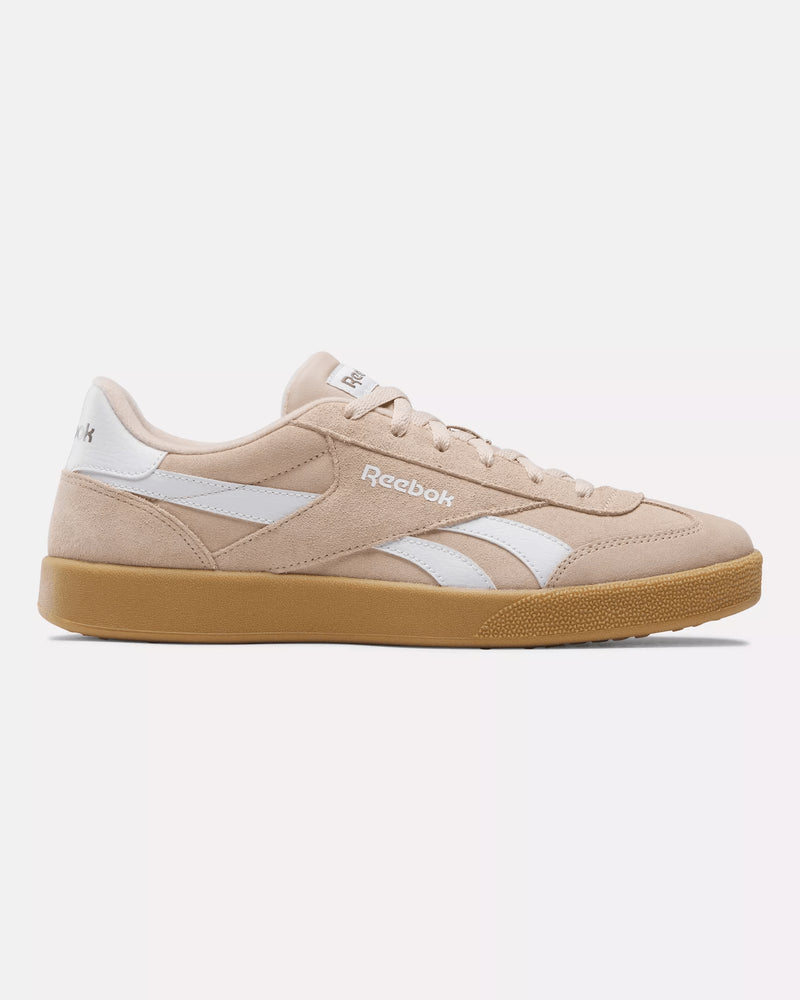 Side view of beige pink Reebok sneakers with white logo details and gum outsole, featuring a classic retro-inspired design.